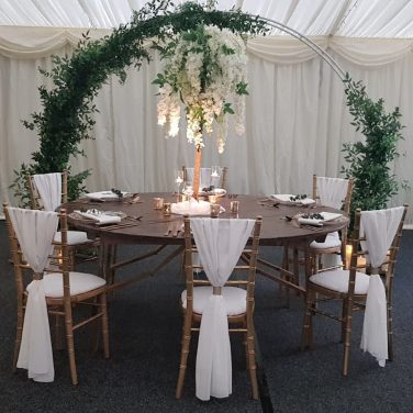 Moon arch foliage marquee oak round table chiavari chaires white vertical drapes wisteria tree centrepiece