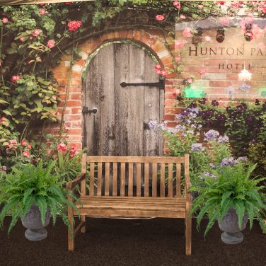 Urns with ferns infront of secret garden backdrop with bench