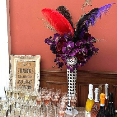 Circus Centrepiece Harlequin Vase with Purple & Red flowers feathers & mirror balls hire rent